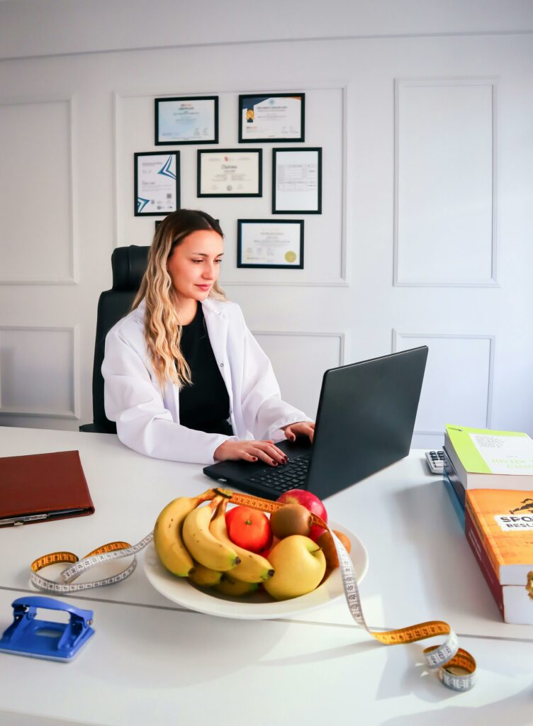 pexels-photo-15391542-15391542 Nutritionist working at desk with laptop and healthy fruits in office setting.