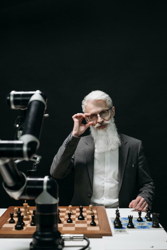 pexels-photo-8438928-8438928 A senior scientist in a suit playing chess with an articulated robot arm on a dark background.